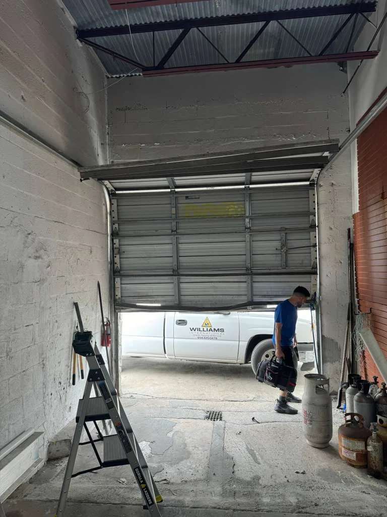 Commercial high-bay warehouse service setup with step ladder and technician inspecting door tracks