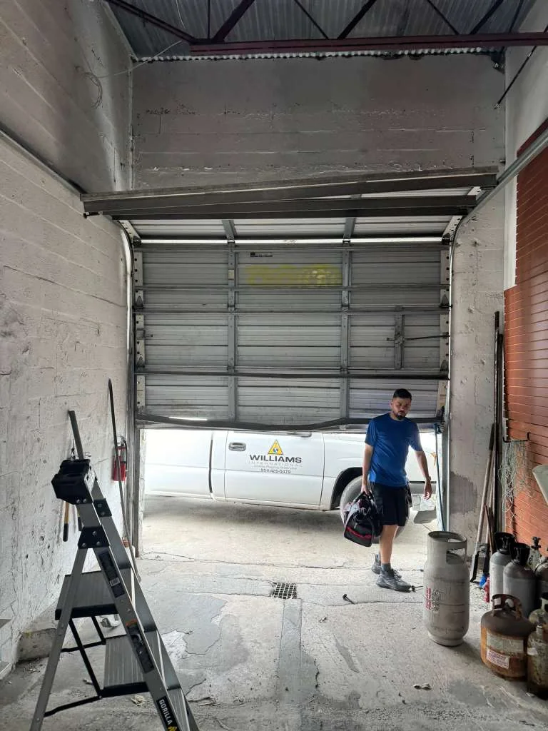 Wide shot of commercial warehouse bay door jammed at angle with technician on site