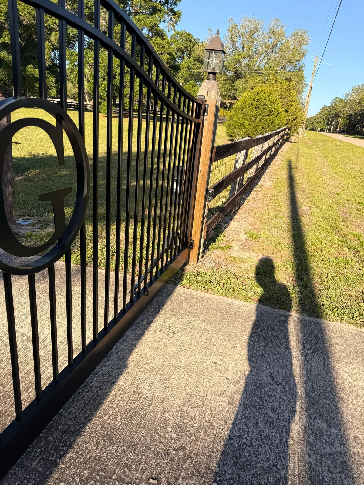 Custom black ornamental wrought iron driveway entrance gate with security hinges and wooden fencing