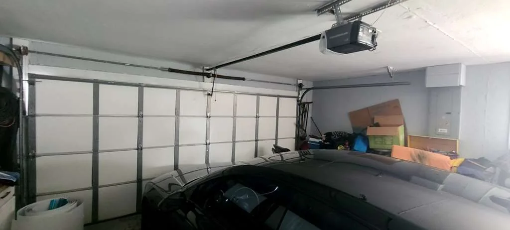 Interior view of closed insulated double garage door with overhead belt-drive motor and vehicle parked inside
