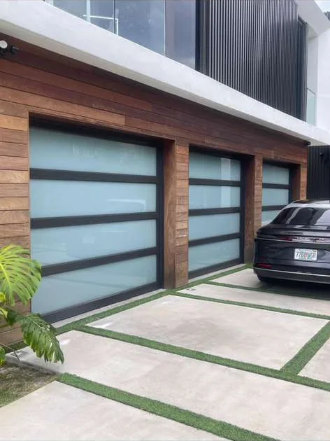 Modern luxury home facade featuring three frosted glass garage doors in teak wood siding with turf driveway