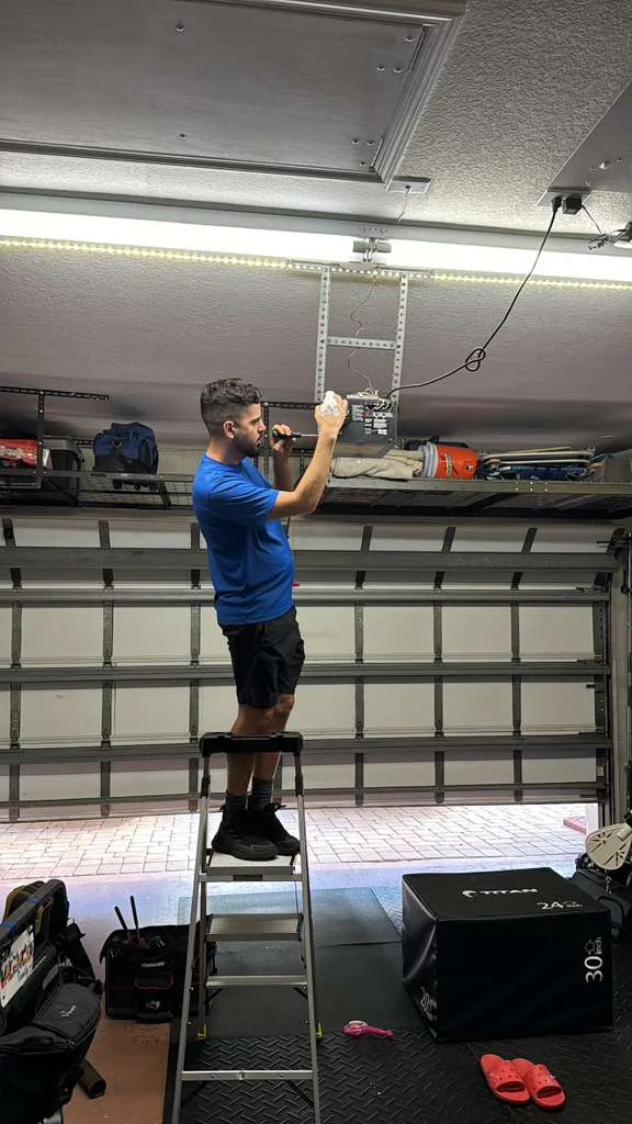 Quick Springs technician standing on ladder wiring overhead garage door opener motor