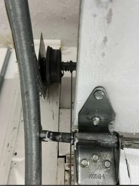 Close-up of garage door lift cable unseated and tangled around cable drum next to track roller hinge