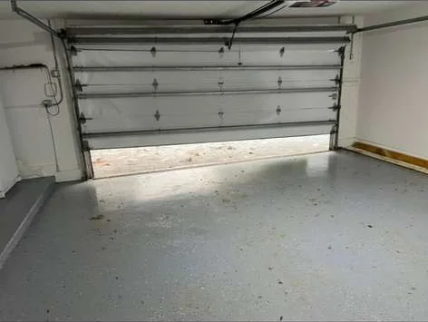 Interior view of residential garage door jammed crooked in track above epoxy floor