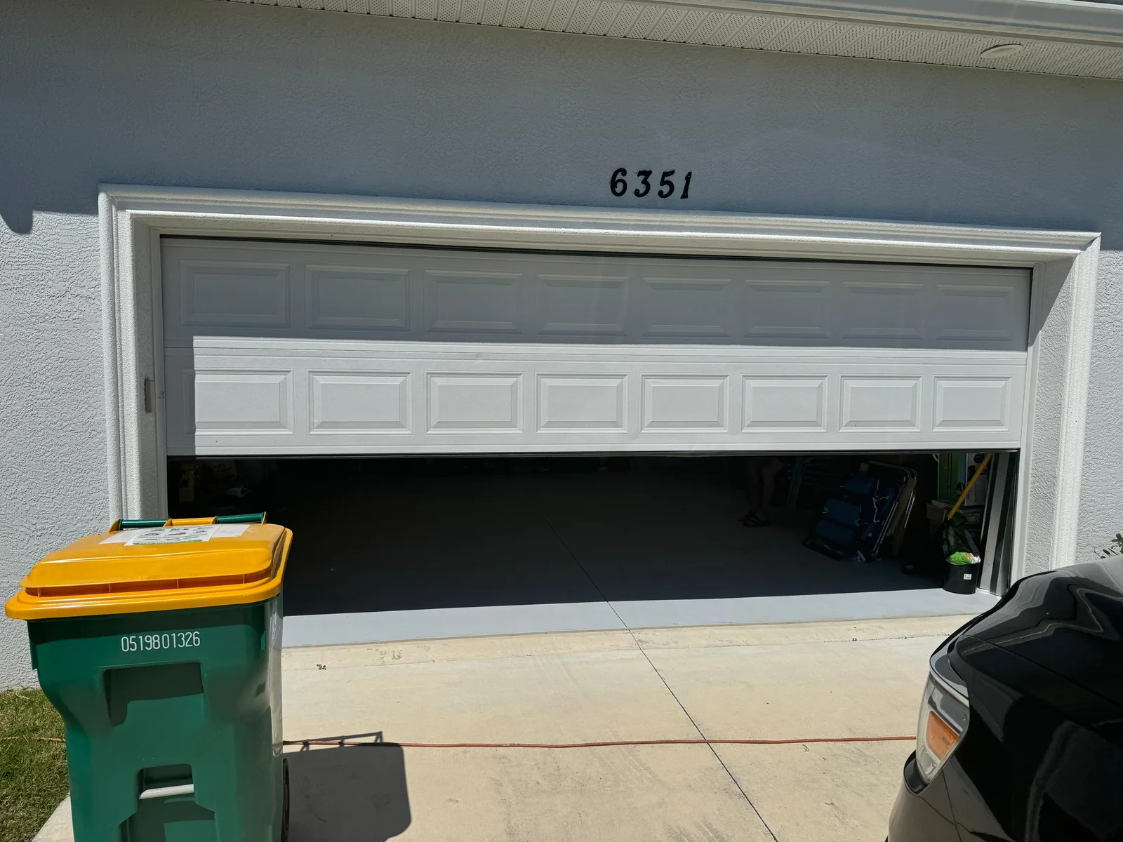 Exterior view of white residential garage door jammed crooked and off-track in Sarasota