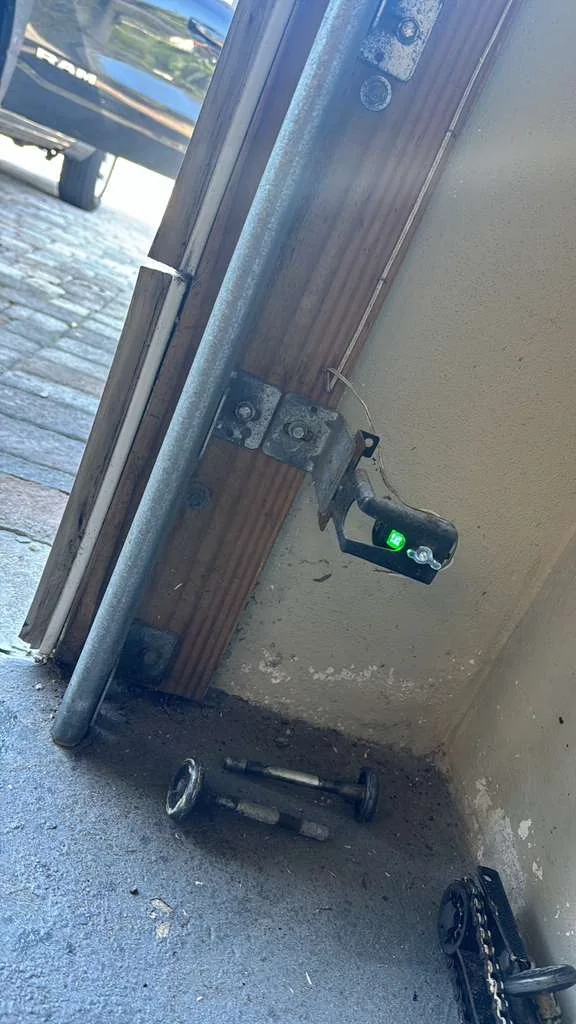 Garage door vertical track with active green safety sensor and replaced worn steel rollers on floor