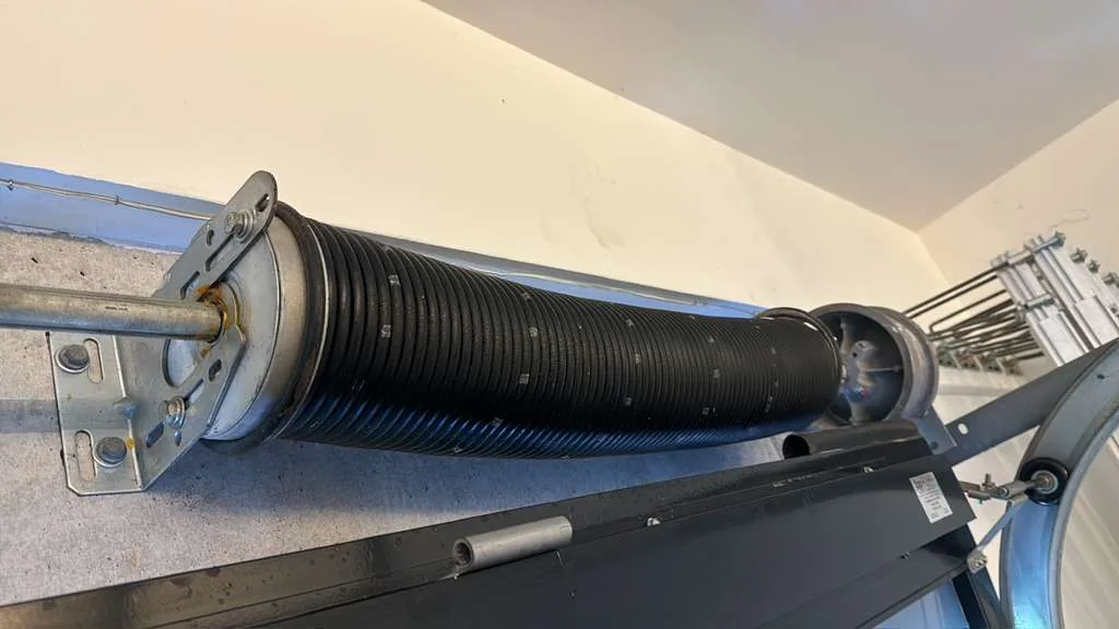 Close-up of heavy-duty torsion spring, winding cone, cable drum, and torsion shaft hardware